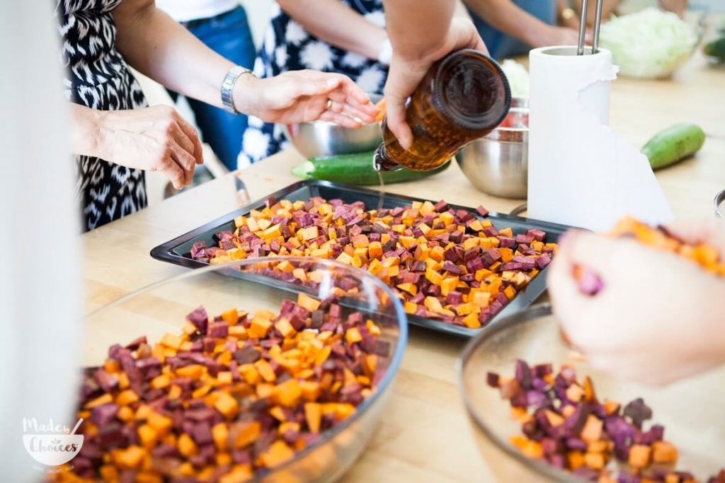 Mãos a preparar batata doce roxa e laranja em cubos num tabuleiro