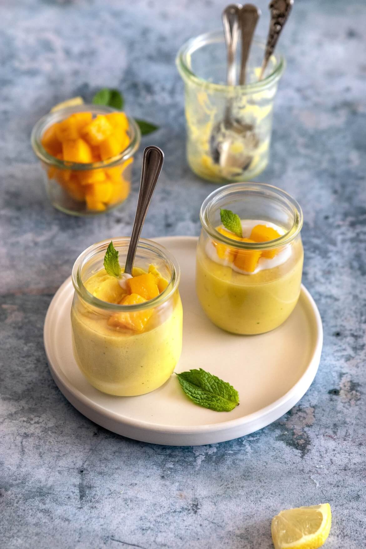 2 taças de vidro num prato com mousse de manga e uma colher