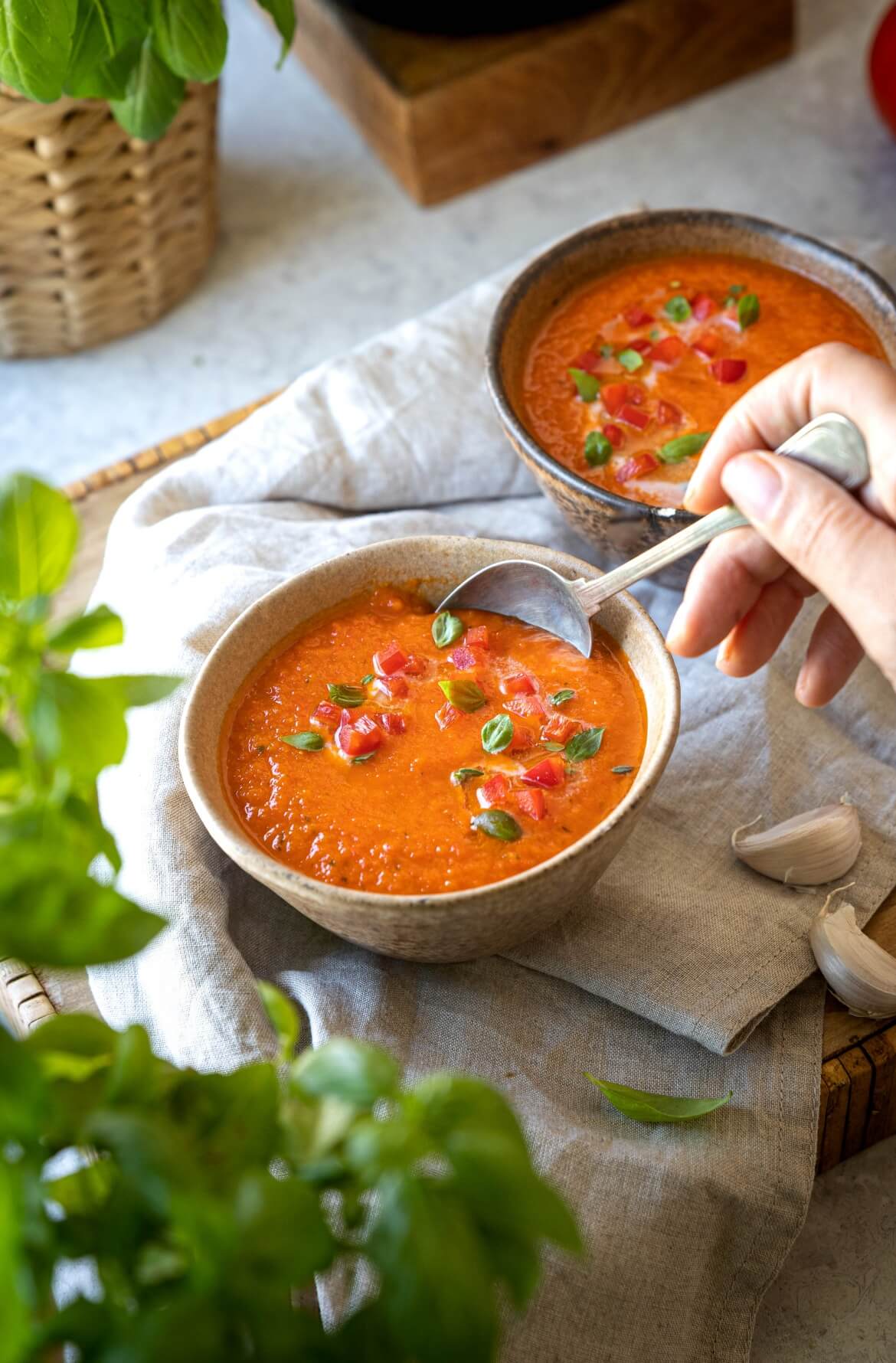 2 taças com sopa de pimentos assados uma mão a segurar uma colher com sopa