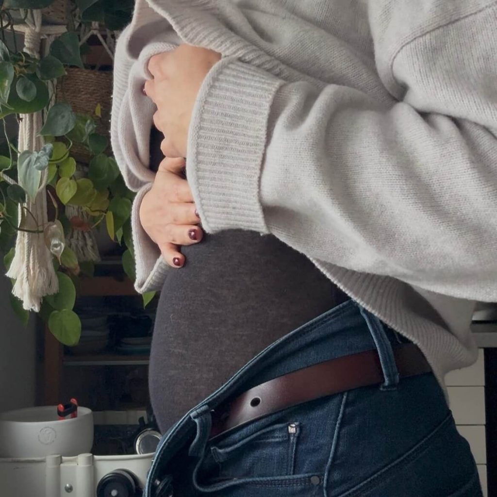 Barriga inchada vista de perfil, com camisola cinzenta e calças de ganga